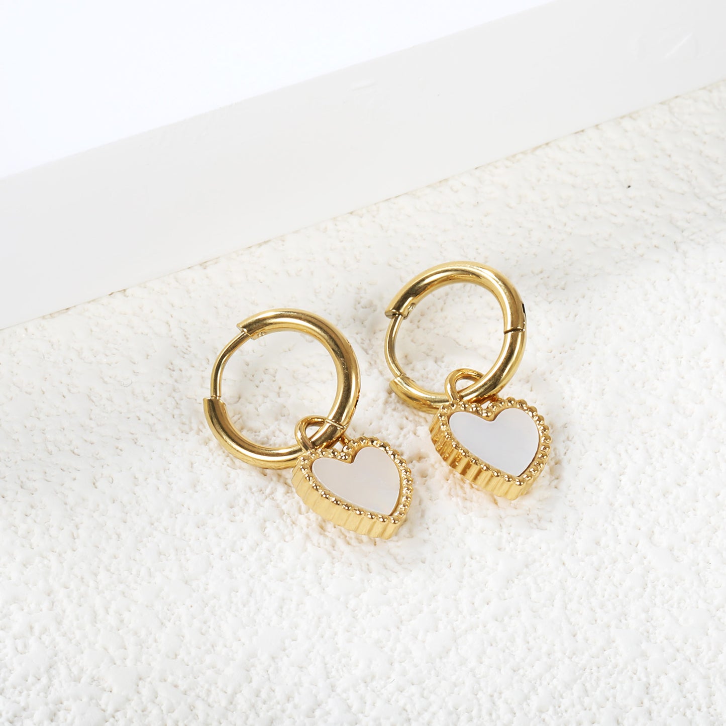 Wholesale stainless steel round pearl heart-shaped earrings with white shell decoration.